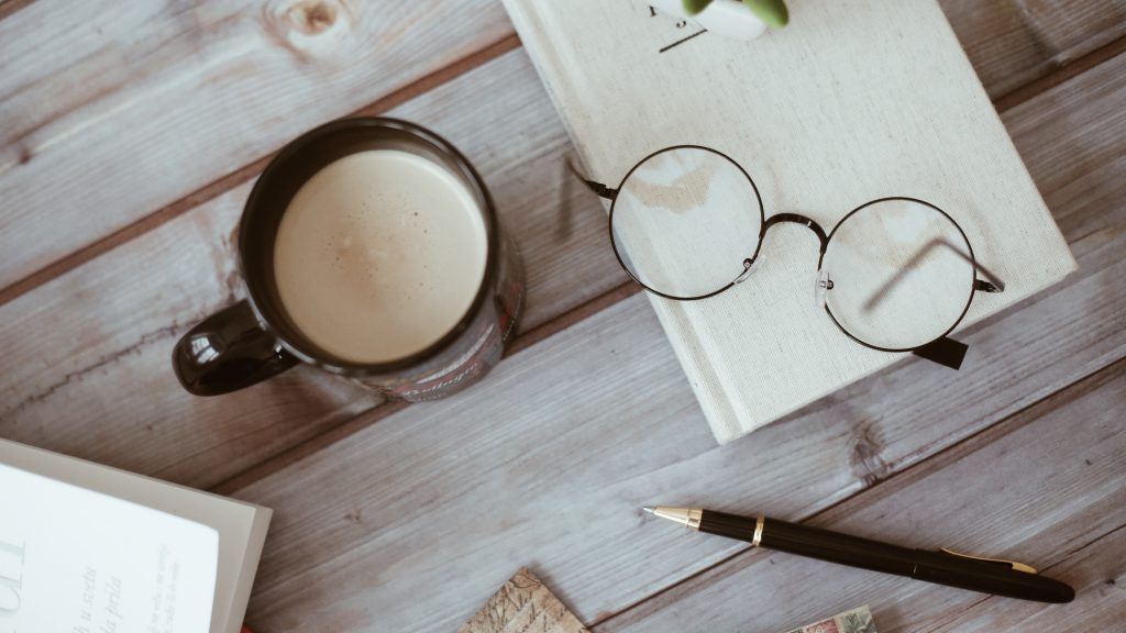 okulary, kawa, długopis i notatnik położone na stole