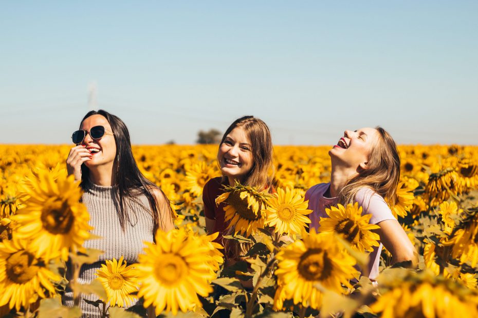 Trzy śmiejące się dziewczyny stojące na łące słoneczników