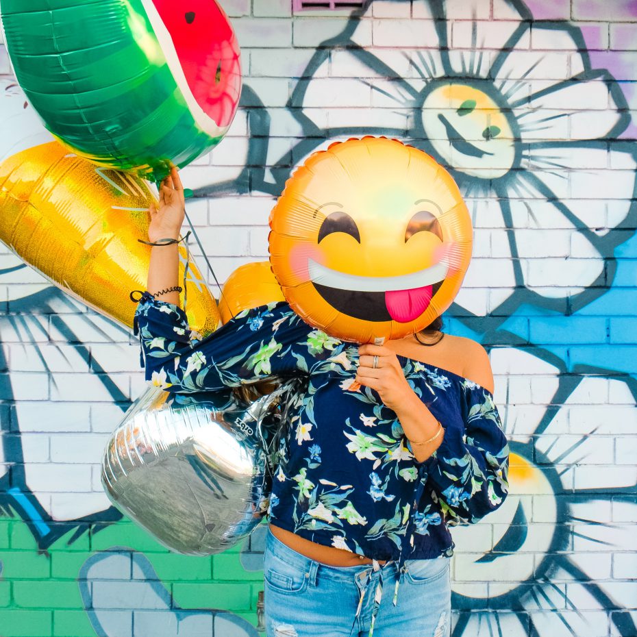 Kobieta zasłaniająca twarz balonem z uśmiechniętą emotikonką